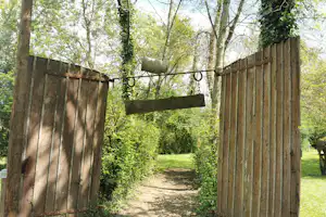 Holzlattenzaun und schmaler Weg im Grünen, umgeben von Bäumen und Sträuchern auf einem Campingplatz.