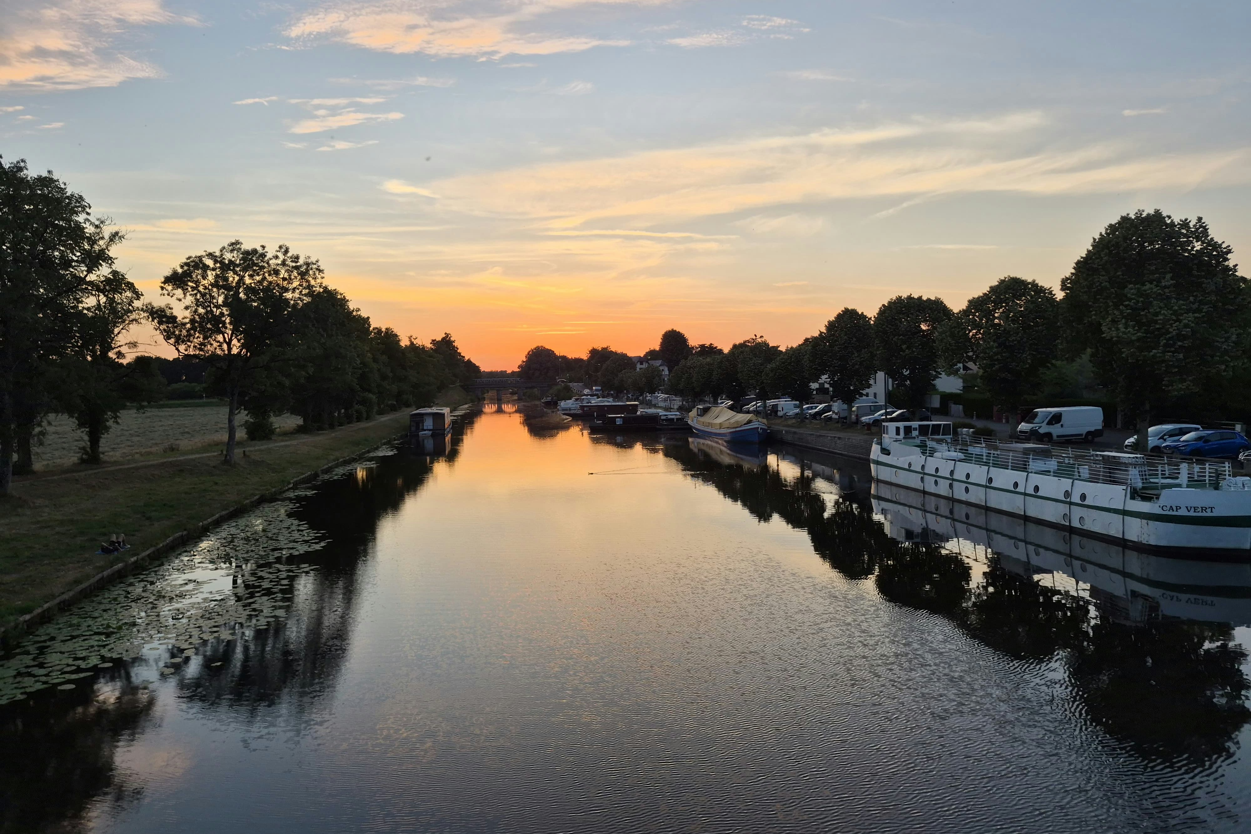 Kanal am Campingplatz mit Booten am Ufer, Bäume und Rasenflächen, im Abendlicht.