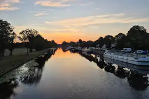 Kanal am Campingplatz mit Booten am Ufer, Bäume und Rasenflächen, im Abendlicht.