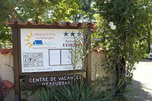 Camping-Infotafel „en Campagne“ mit Öffnungszeiten und „Centre de Vacances d’Essubras“ vor Bäumen und Kiesweg.