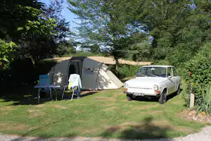 Campingzelt auf dem Rasen neben einem Auto, mit Campingstuhl und Tisch, umgeben von Bäumen und Hecken.