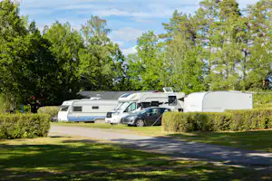 Wohnmobile und ein Campingbus stehen auf einem Stellplatz zwischen Hecken und Bäumen, im Hintergrund ein weiteres Fahrzeug.