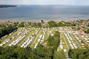 Luftaufnahme eines Campingplatzes am See mit vielen Stellplätzen, Wohnwagen und Zelten, umgeben von Bäumen und Wegen.