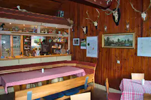 Holzraum mit Theke und Regalen, daneben Tische mit karierten Decken und Stühlen, an der Wand Bilder und Schilder.