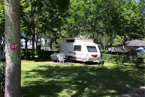 Wohnmobil auf einem Stellplatz im Grünen, mit Tisch und Stühlen vor dem Fahrzeug, umgeben von Hecken und Bäumen.