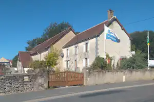 Weißes Gebäude mit Satteldach und Flagge am Eingang, Steinmauer und Holzzaun entlang der Straße.