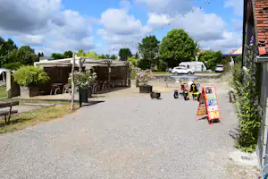 Schotterweg am Campingplatz mit Terrasse, Sitzgarnitur und Wohnwagen; im Hintergrund Bäume und ein Auto.
