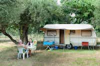 Camping Gythion Bay - Camper sitzen vor dem Wohnmobil im Schatten der Bäume auf dem Campingplatz