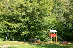 Spielplatz im Grünen: Schaukel, Rutsche und Federwippe vor dichtem Baumbestand auf dem Campinggelände.