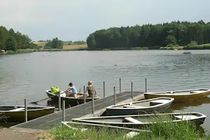 Ruderboote am Seeufer am Campingplatz, im Vordergrund mehrere Boote und ein Steg mit Geländer.
