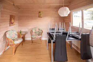 Essbereich in einem Holzblockhaus mit Tisch, Stühlen und Sitzbank, daneben Fenster und Holzdecke.
