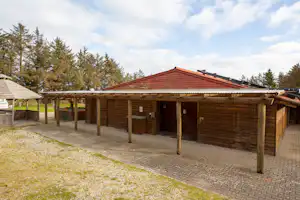 Holz-Carport am Campingplatz mit überdachter Terrasse, gepflastertem Boden und Blick auf Bäume im Hintergrund.