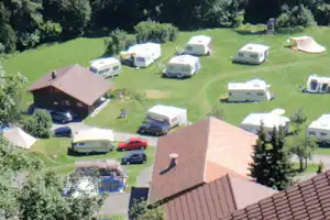 Blick auf einen Campingplatz mit Wohnwagen und Zelten auf grünen Stellplätzen, nahe einem Gebäude und einem Pool.