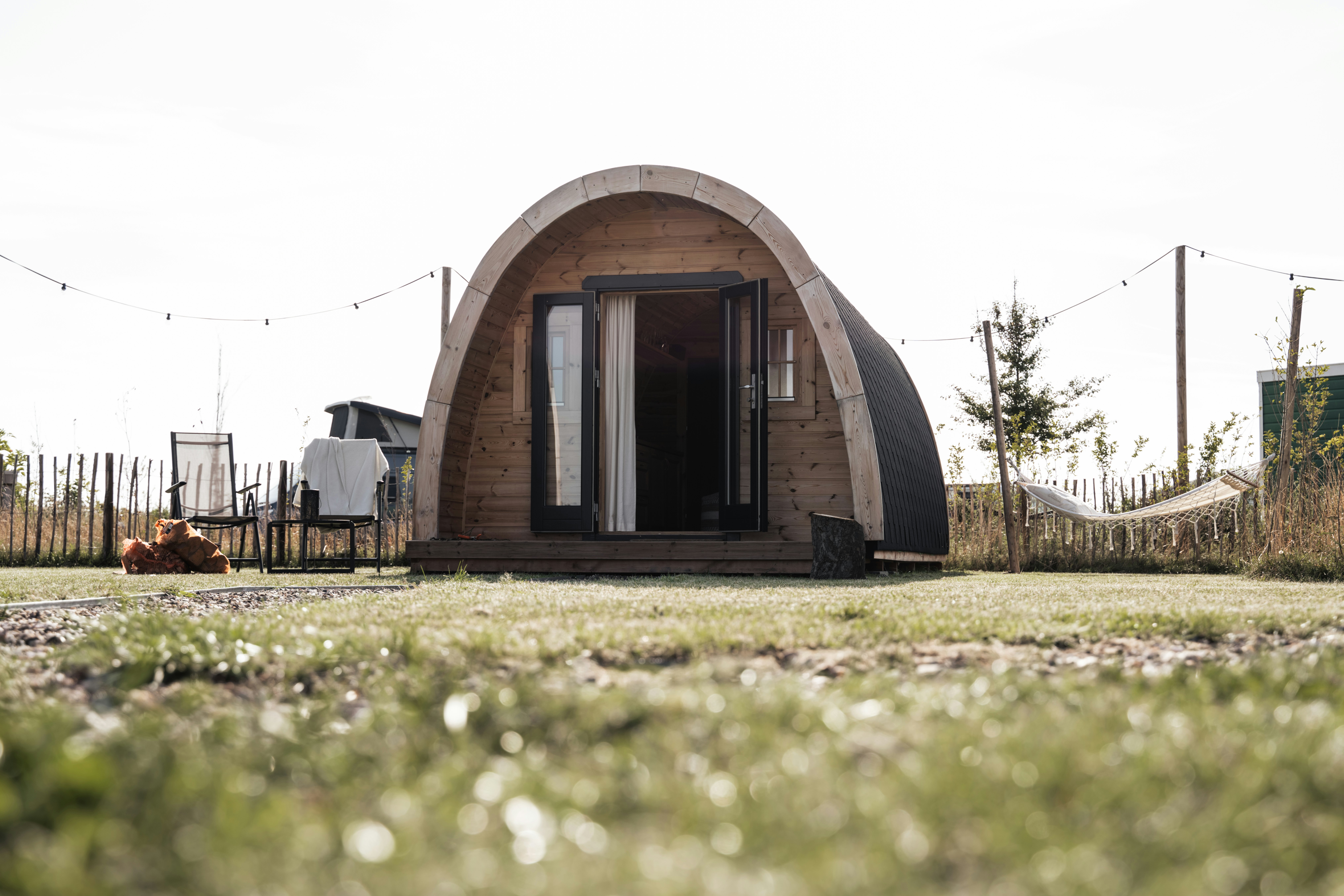 Rundes Holz-Glampinghaus mit großen Fenstern auf einem Campingplatz, im Vordergrund Gras und ein Weg.