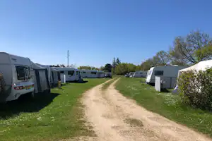 Reihe von Wohnwagen und Zelten auf einem Campingplatz, Grasflächen und ein Schotterweg zwischen den Stellplätzen.