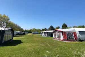 Campingplatz mit Rasenfläche, roten und weißen Zelten sowie Wohnwagen und Autos am Rand.