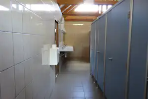 Flur im Camping-Badezimmer mit Waschbecken, weißen Fliesen, grauen Türen und Holzdecke im Hintergrund.