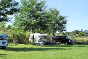 Wohnwagen und Zelt auf dem Campingplatz, daneben ein Auto, Sitzgruppe unter Bäumen im grünen Garten.