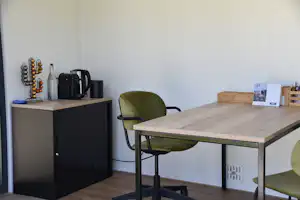 Wohnbereich in einem Camping-Mobilheim: Esstisch mit Stühlen, Küchenzeile mit Kaffeemaschine und Schrank, Holzfußboden.