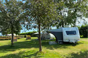 Wohnwagen mit Vorzelt auf einem Campingplatz, umgeben von Rasen, Hecken und Bäumen.
