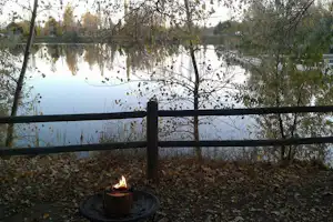 Feuerschale am Campingplatz am See, umgeben von Laub und Bäumen, mit Blick auf das ruhige Wasser.