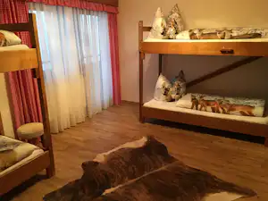 Zwei Etagenbetten mit Kissen und Decken, Holzboden und Vorhang am Fenster in einem Campingzimmer.