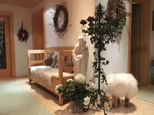 Bett in einem Wohnbereich mit Holzrahmen, weißem Fellteppich und dekorativen Pflanzen an einer Metallständer- Ecke.