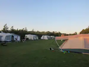 Zelte auf einem grünen Campingplatz, im Hintergrund weitere Wohnwagen und Zelte, Stühle und ein Tisch am Stellplatz.