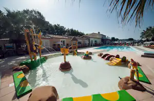 Familienpool mit mehreren bunten Liegen, Palmen und Blick auf das Poolgebäude und weitere Sitzbereiche am Rand.