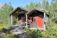 Camping Hov Hyttegrend - Holzhütte mit Terrasse und Sofa zwischen den Bäumen auf dem Campingplatz