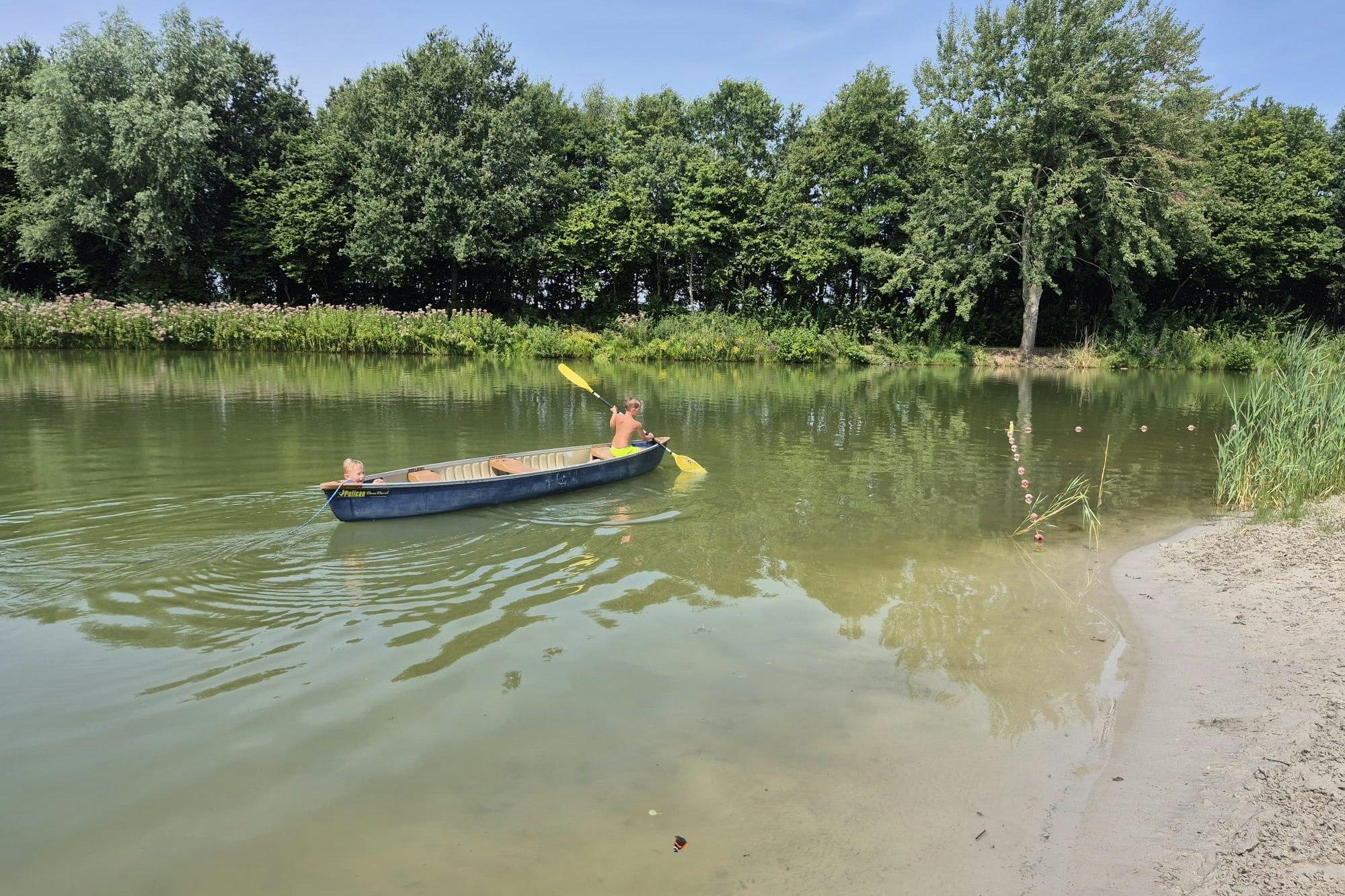Ein Schlauchboot treibt auf einem ruhigen See, am Ufer mit Gras und Bäumen im Hintergrund.