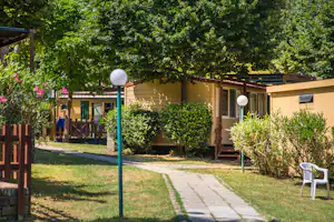 Bungalow im Grünen mit Terrasse, Hecken und Gartenweg, umgeben von Bäumen und Sträuchern.