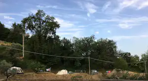 Zelte auf einem Campingplatz am Hang, umgeben von Bäumen, mit Wäscheleine und Pfosten im Vordergrund.