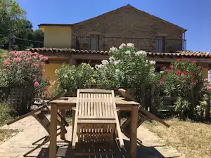 Holztisch und Stühle auf einer Terrasse mit Blumenbeeten vor einem Campinghaus mit Holzfassade und Fensterläden.