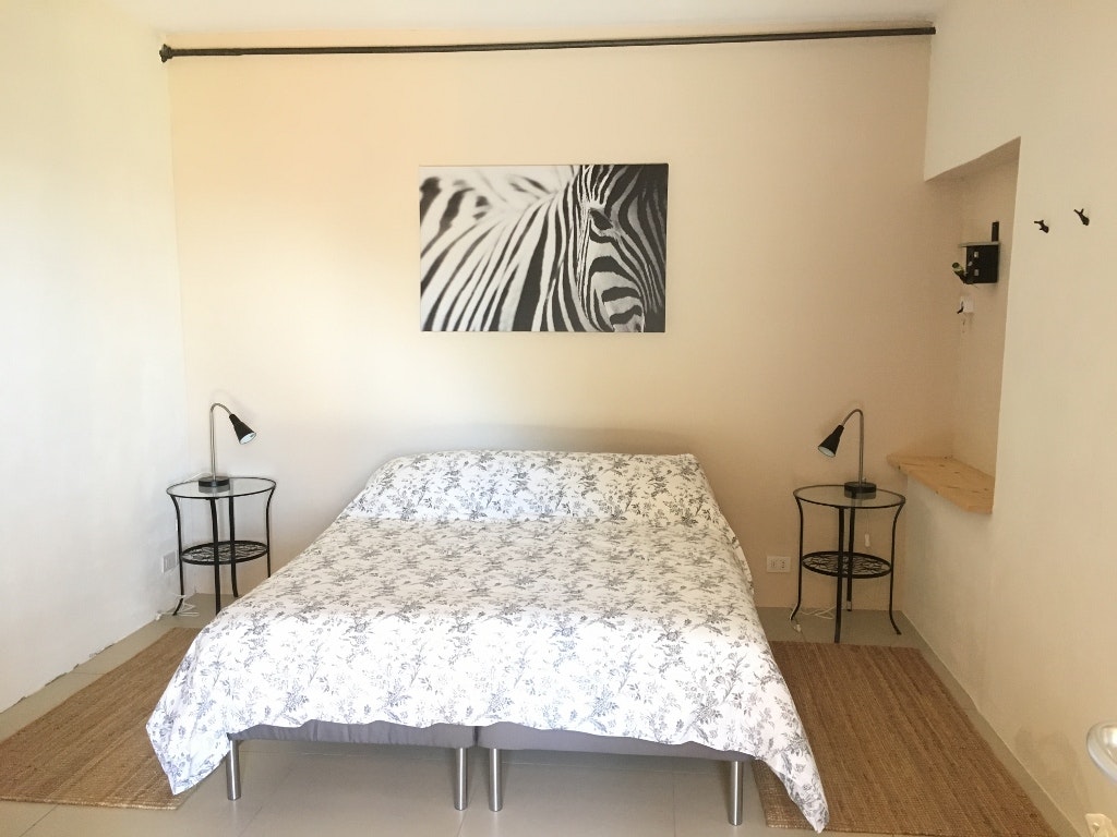 Bett in einem kleinen Schlafzimmer der Campingunterkunft, mit Nachttischen, Lampen und Zebra-Bild an der Wand.