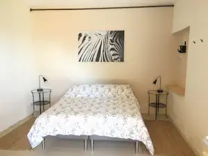 Bett in einem kleinen Schlafzimmer der Campingunterkunft, mit Nachttischen, Lampen und Zebra-Bild an der Wand.