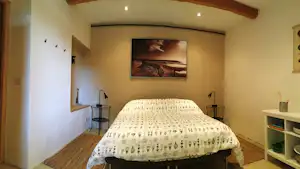 Schlafzimmer im Campinghaus mit Doppelbett, gemusteter Bettwäsche, Nachttischen, Holzdecke und Wandbild.