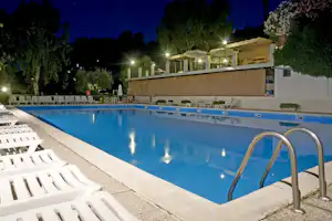 Beheizter Pool am Campingplatz bei Nacht, beleuchtete Liegen und Treppe am Beckenrand, Bäume im Hintergrund.