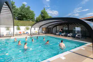 Schwimmbecken im Campingbereich mit Überdachung, Liegestühlen und Sonnenschirmen am Beckenrand, im Hintergrund Bäume und Himmel.