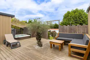 Holzterrasse mit Sitzgruppe, zwei Liegen und kleinem Holztisch, umgeben von Hecken und Sichtschutzzaun.