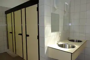 Küchenzeile mit zwei Edelstahl-Spülbecken, Fliesenwand und Schiebetür im Sanitärbereich eines Campinghauses.