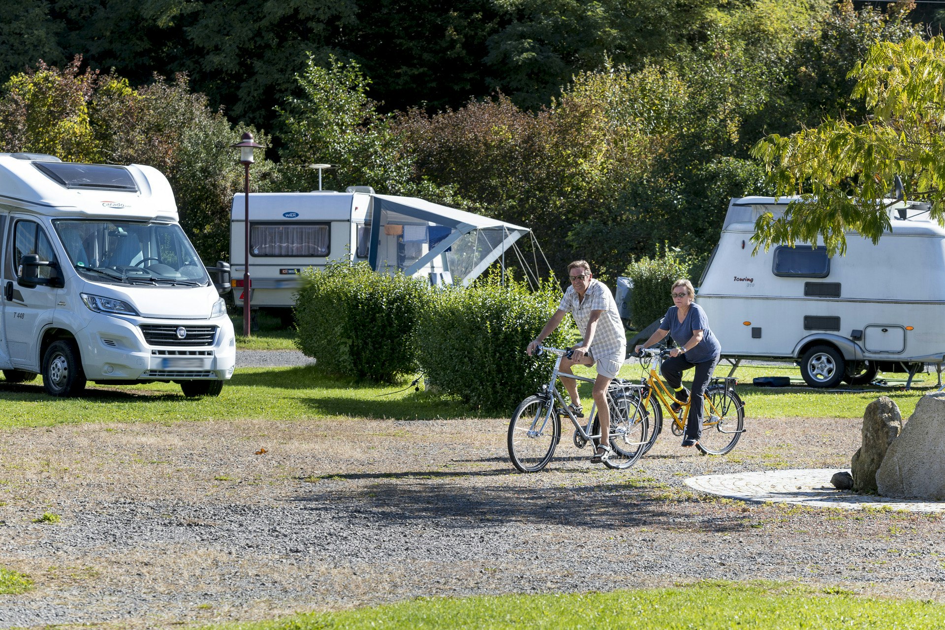 Camping im Thermenland - Radler auf einem Weg des Campingplatzes mit Wohnwagen im Hintergrund