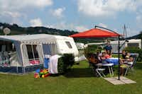 Camping im Thermenland - Wohnwagen auf einem Stellplatz mit Campern, die unter einem Sonnenschirm sitzen