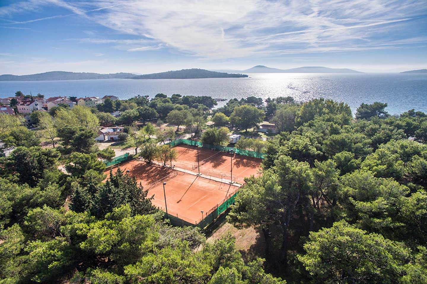 Camping Imperial - Luftaufnahme auf Tennisplätze des Campingplatzes mit einer Bucht des Mittelmeers im Hintergrund