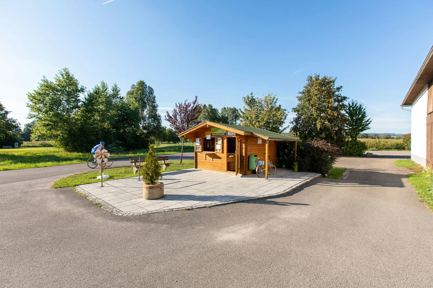 Holz-Rezeption auf dem Campingplatz mit gepflasterter Terrasse, Fahrrädern und Bäumen im Hintergrund.