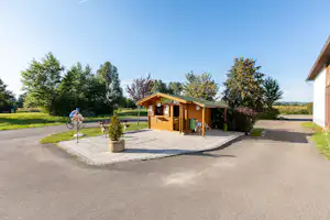 Holz-Rezeption auf dem Campingplatz mit gepflasterter Terrasse, Fahrrädern und Bäumen im Hintergrund.