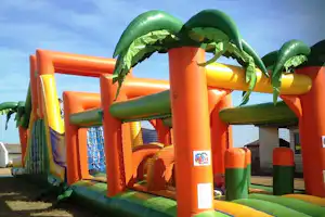 Aufblasbare Kinder-Hüpfburg mit orange-grünen Wänden und Netzfenstern auf dem Campingplatz, im Hintergrund ein Zaun.