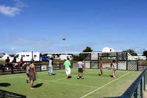 Fußballfeld auf dem Campingplatz mit Kunstrasen, Umzäunung und mehreren Wohnmobilen im Hintergrund.