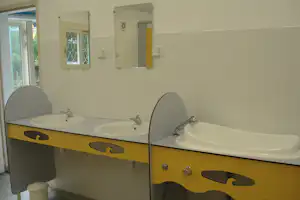 Camping-Badezimmer mit zwei Waschbecken, gelber Waschtischfront, Spiegeln und Fliesenwand.