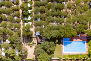 Luftaufnahme eines Campingplatzes mit vielen Stellplätzen, Bäumen und einem großen blauen Pool im rechten Bereich.